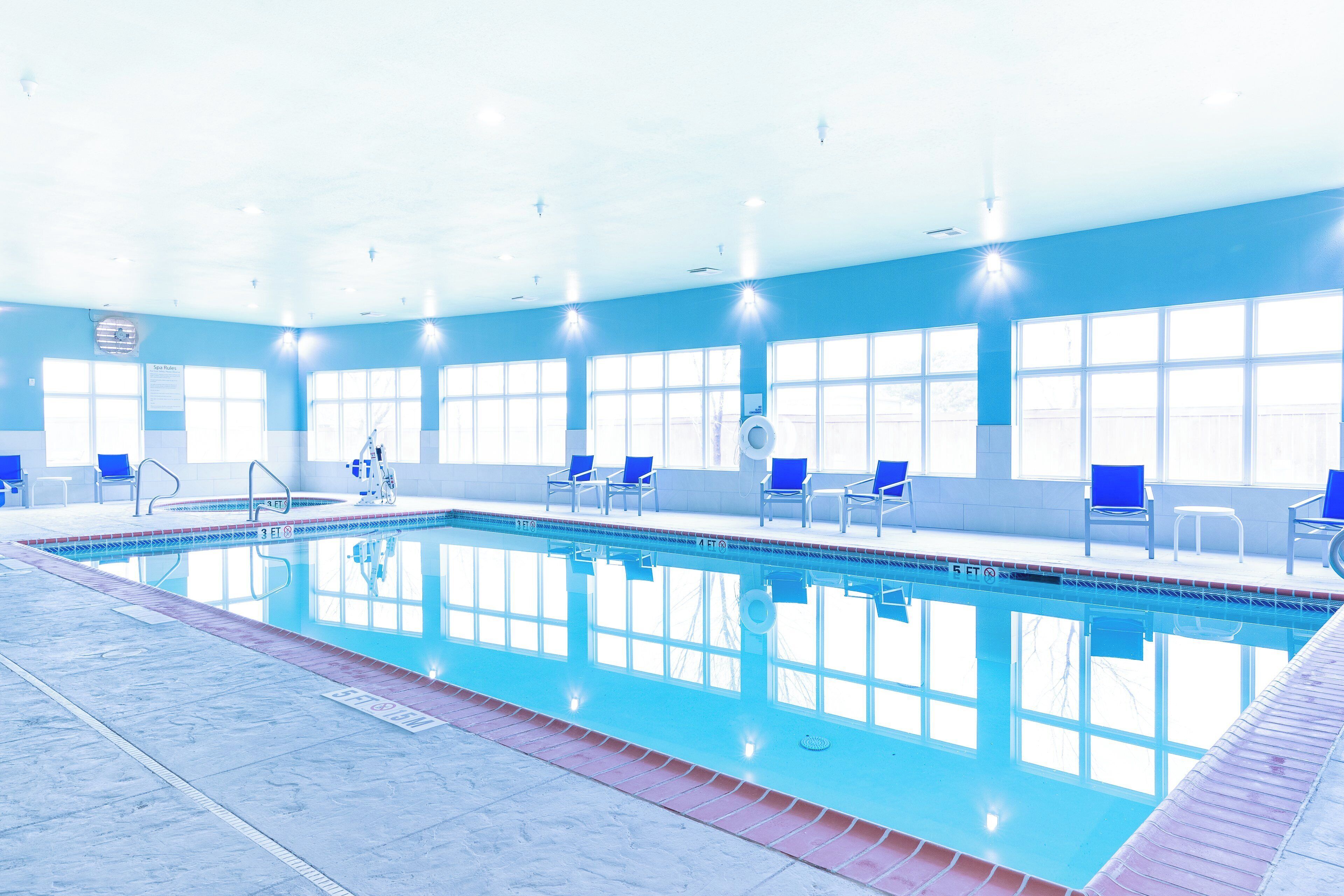 Piscina interna com água cristalina, cadeiras azuis e um ambiente iluminado por luz solar com amplas janelas.