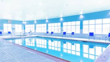 Piscina interna com água cristalina, cadeiras azuis e um ambiente iluminado por luz solar com amplas janelas.