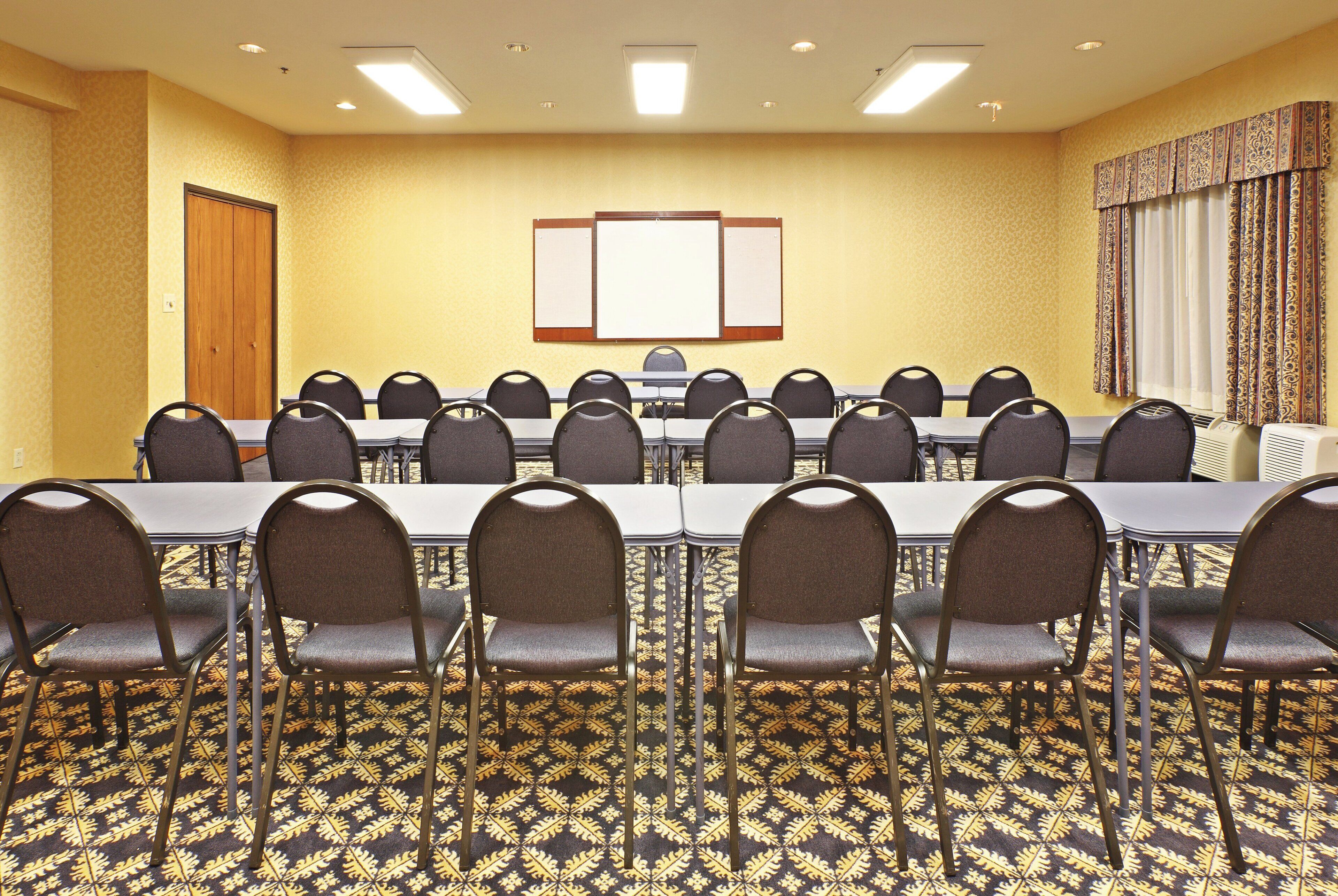 A conference room with a long table, multiple chairs, a bulletin board, and patterned carpet.