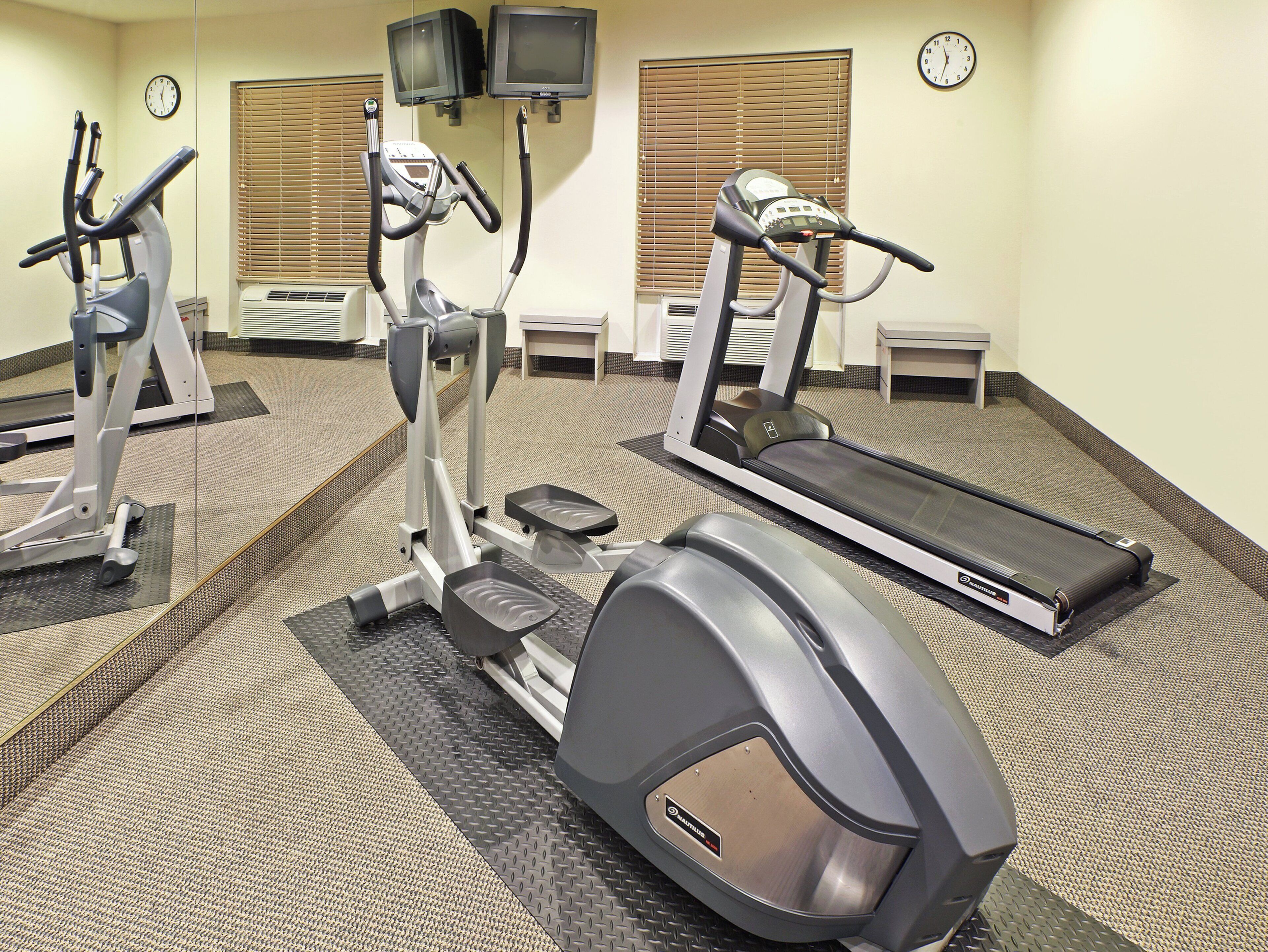 A gym with treadmills, stationary bikes, and a mirrored wall.