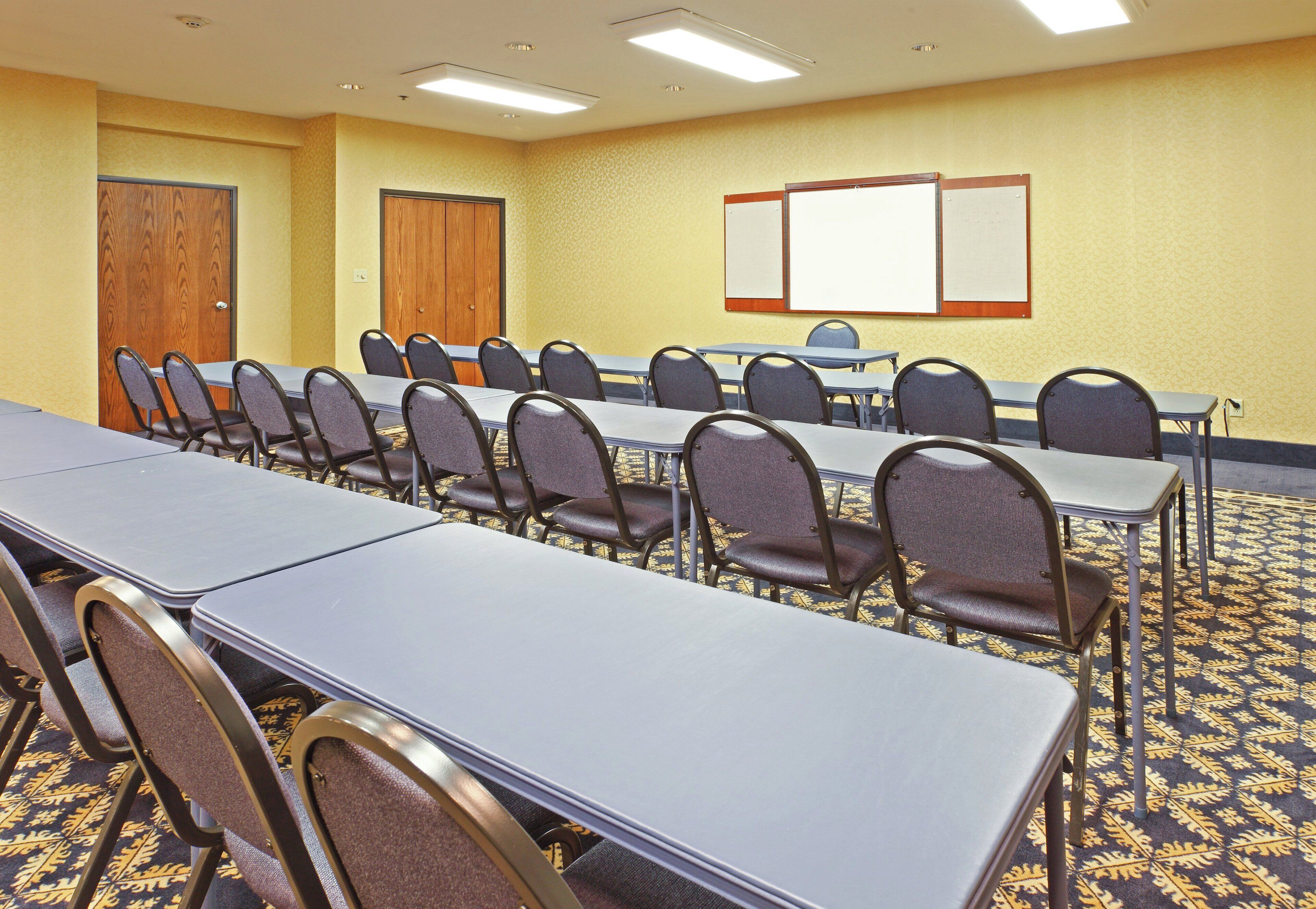 Un salón de conferencias con varias mesas y sillas, una puerta de madera y tablones de anuncios en la pared.