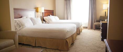 A hotel room with two beds, a desk, a chair, and a lamp.