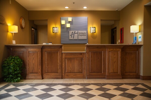 A reception area with a checkered floor, wooden reception desk, wall-mounted clock, and Holiday Inn Express signage. - Holiday Inn Express Hotel & Suites Mountain Home by IHG (Mountain Home)