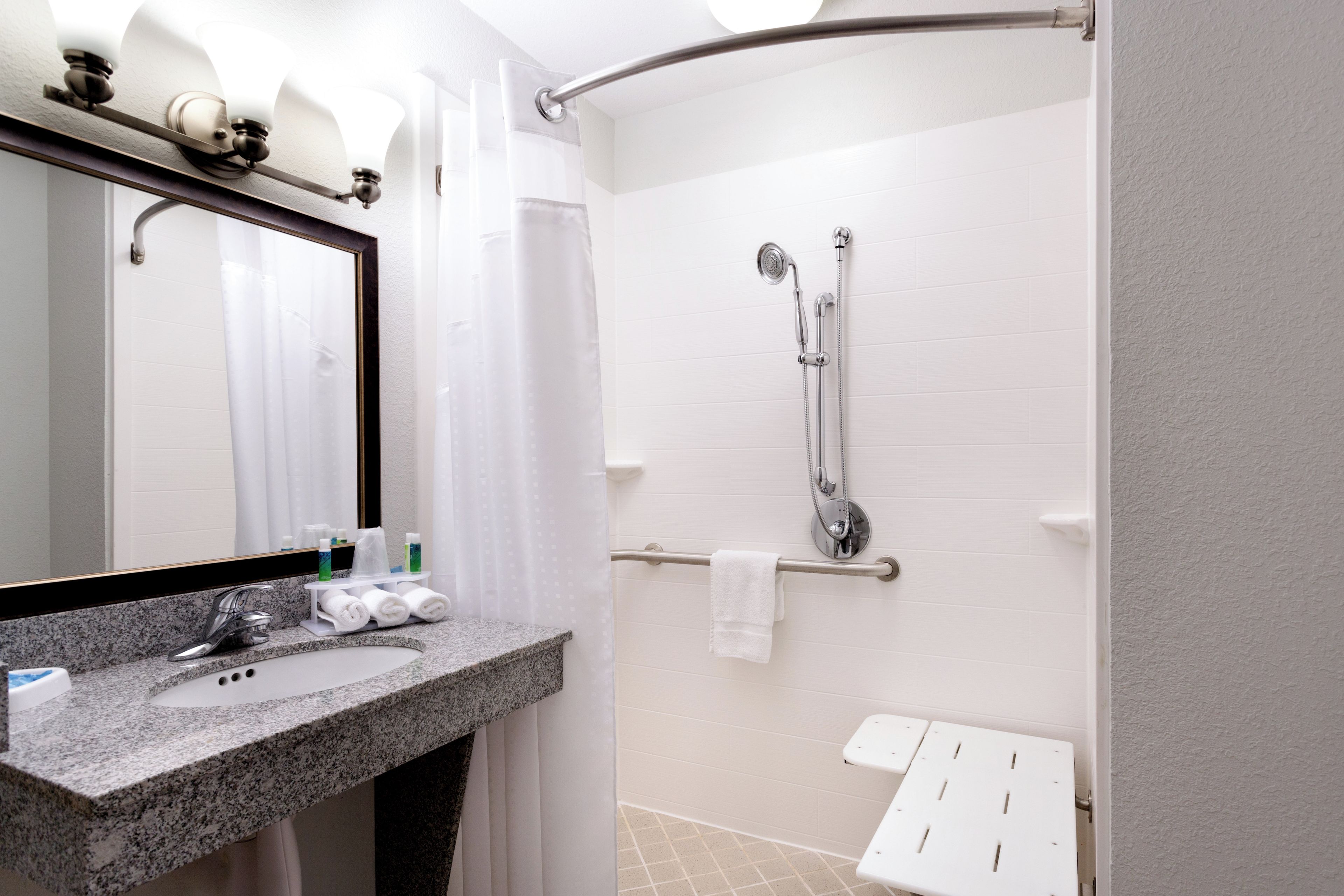 Een badkamer met een wastafel met een granieten blad, een spiegel, een douche met een handdouche en een handdoekhouder.