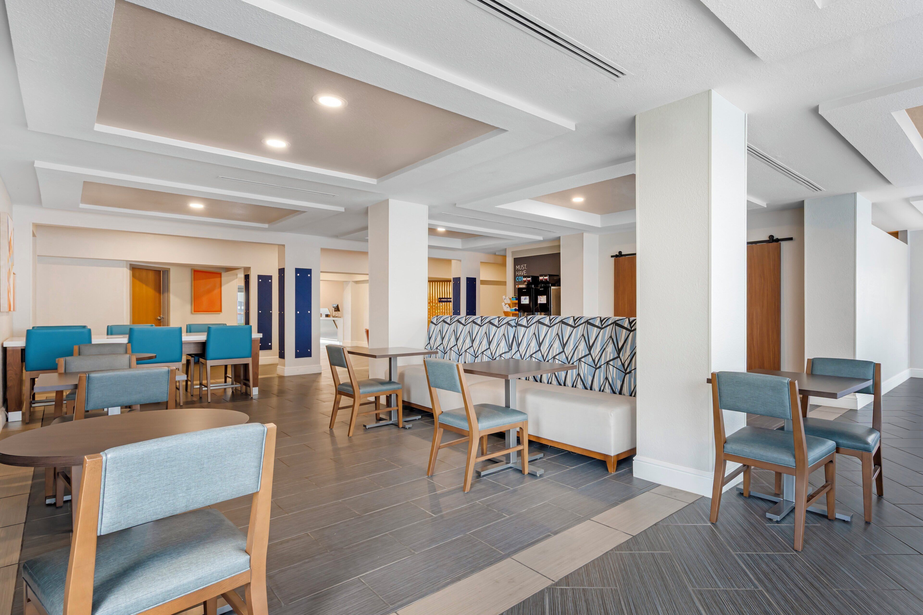 A modern hotel lobby with multiple seating areas, including tables and chairs, and a central seating area with a patterned backrest.