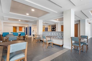Un hall d’hôtel moderne doté de plusieurs espaces de détente, notamment des tables et des chaises, ainsi qu’un espace de détente central avec un dossier à motifs.