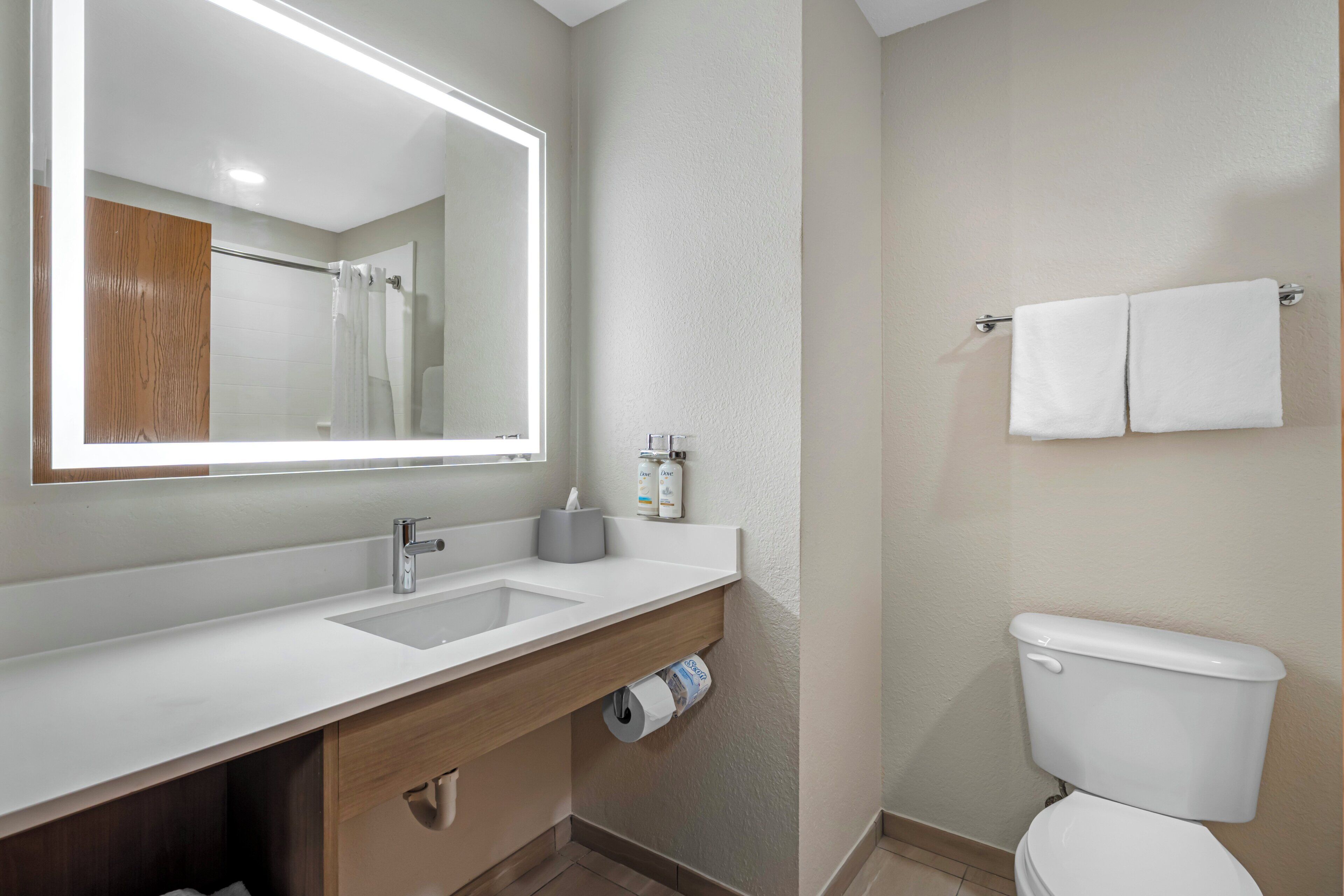 A modern bathroom with a large mirror, a sink, a toilet, and a shower area.