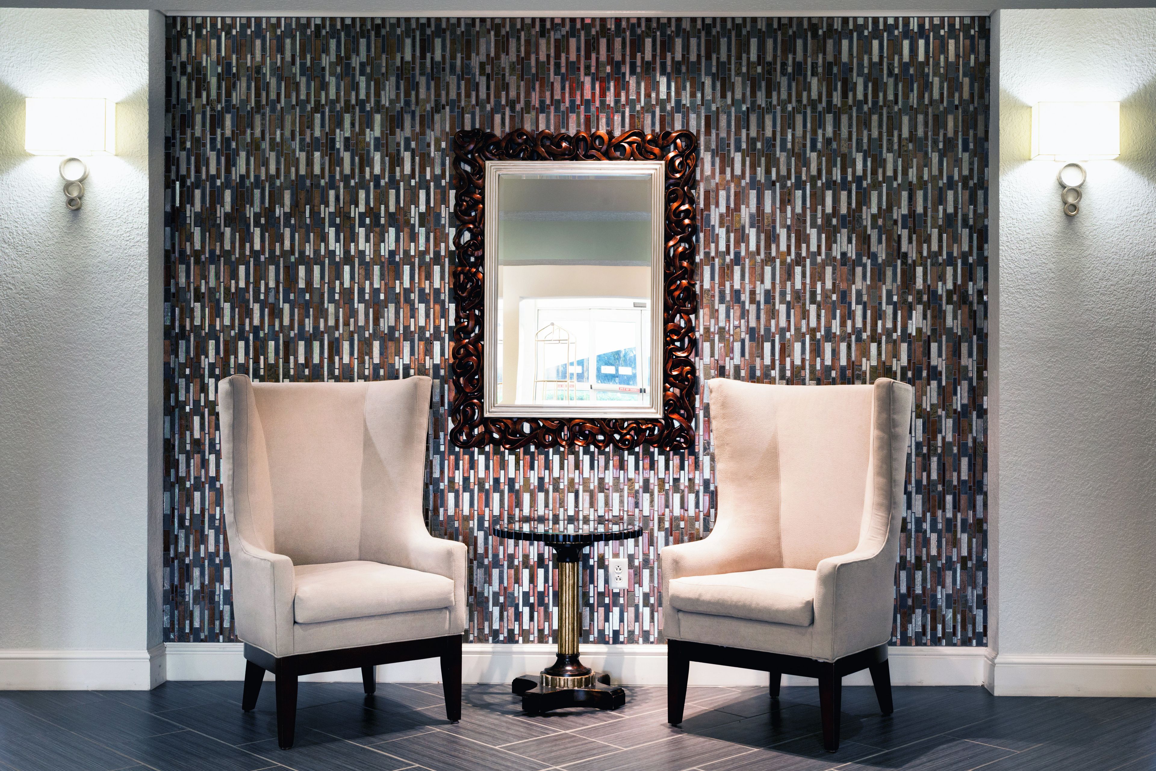 A room with two armchairs, a small table, and a mirror with a geometric patterned wall behind.