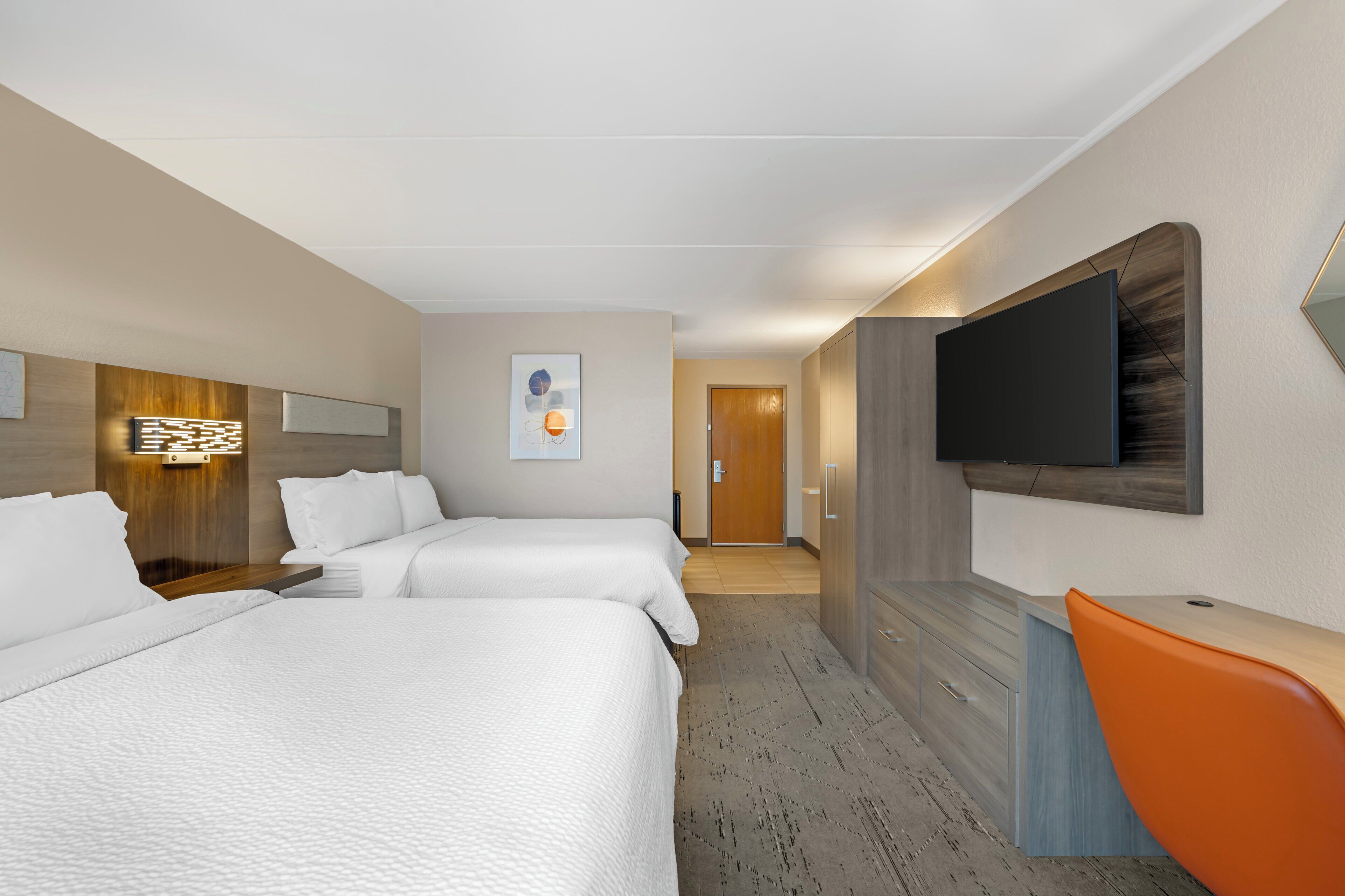 A hotel room with two beds, a desk, a TV, and a bathroom in the background.