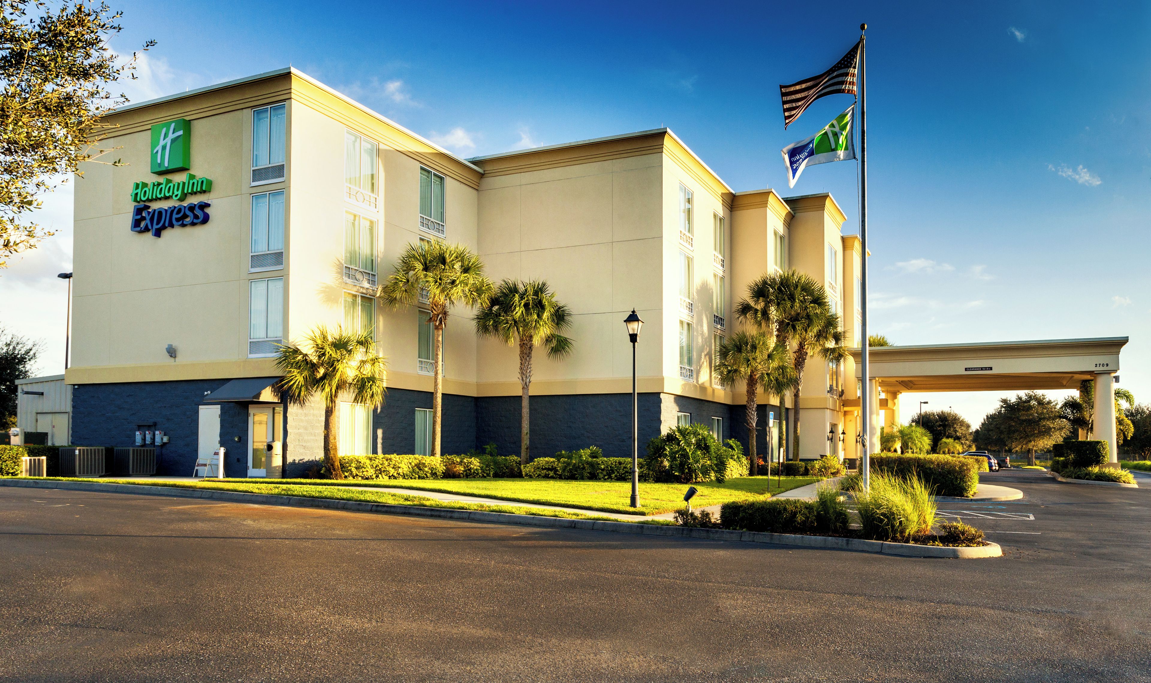 A Holiday Inn Express building with a parking lot, palm trees, and a flag.
