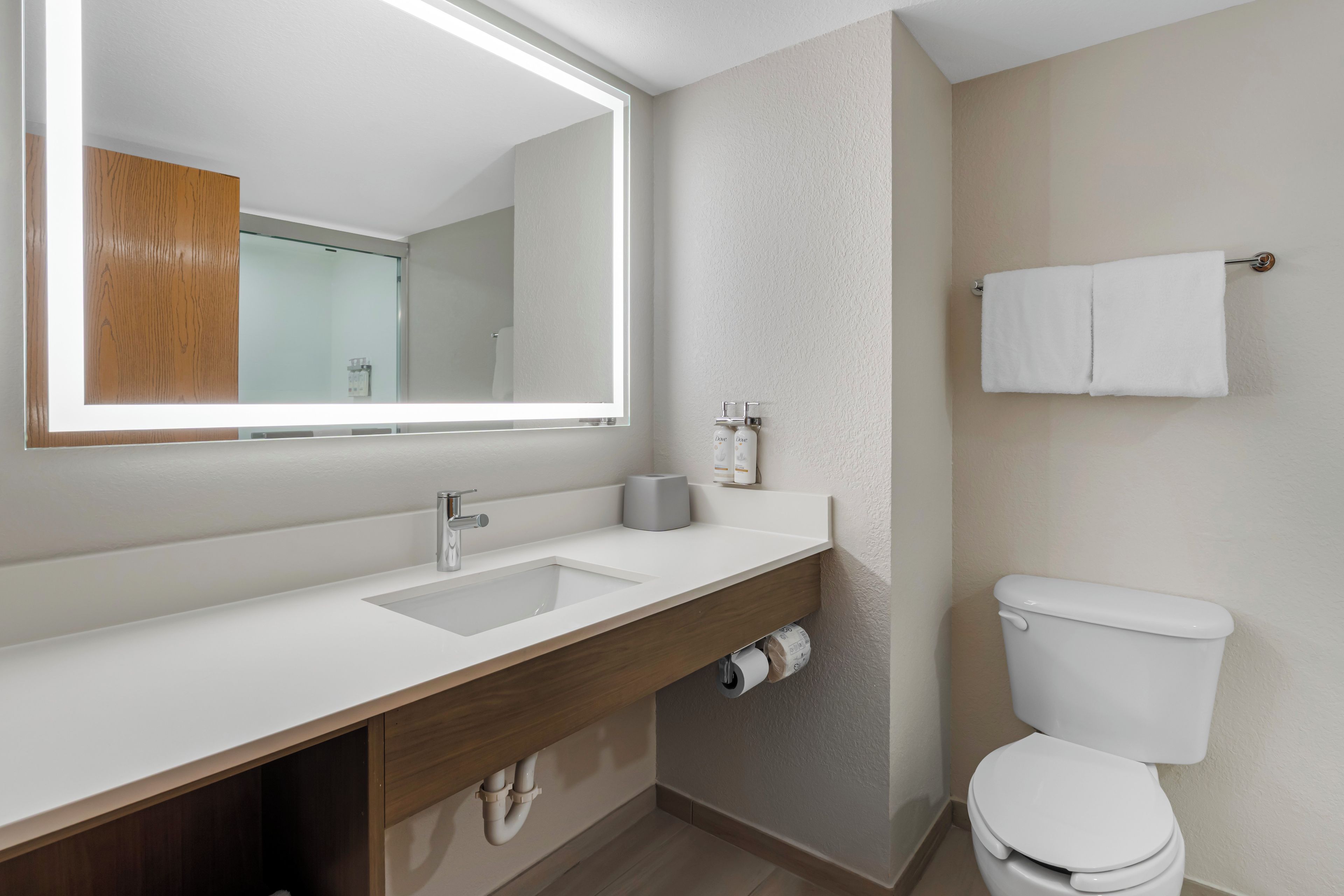 A modern bathroom with a white sink, a large mirror, a toilet, and a towel rack.