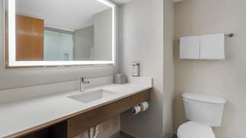 A modern bathroom with a white sink, a large mirror, a toilet, and a towel rack.