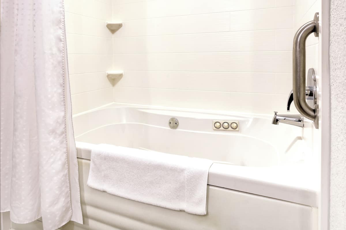 Un baño blanco con una bañera, un cortinón de ducha y una toalla.