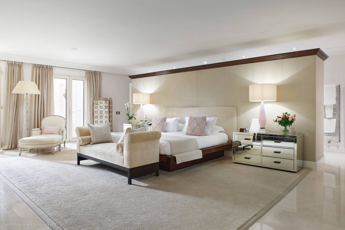 A spacious bedroom with a large bed, a sitting area with a chair, a nightstand, and a dresser.