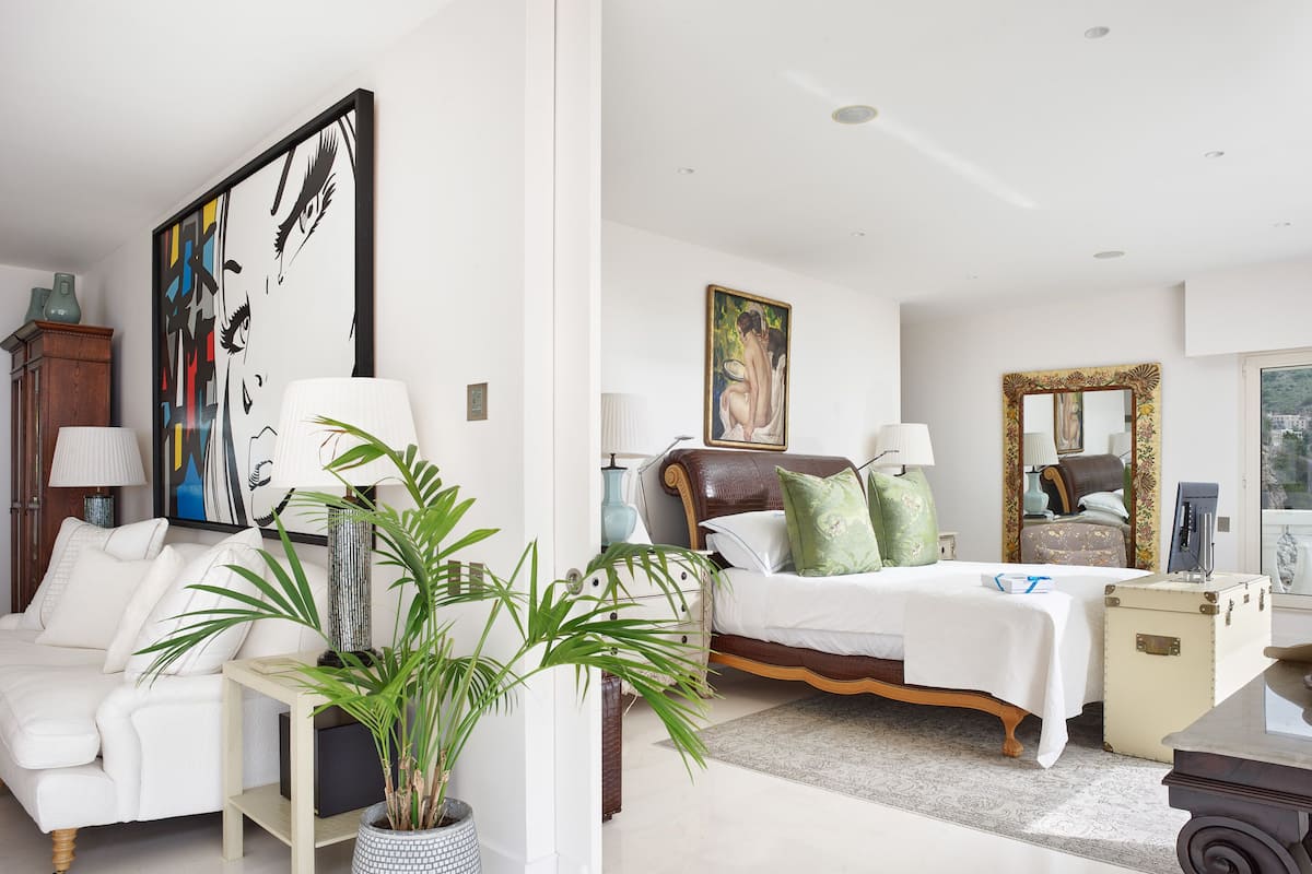 A spacious living room with a white sofa, a large painting, and a potted plant.