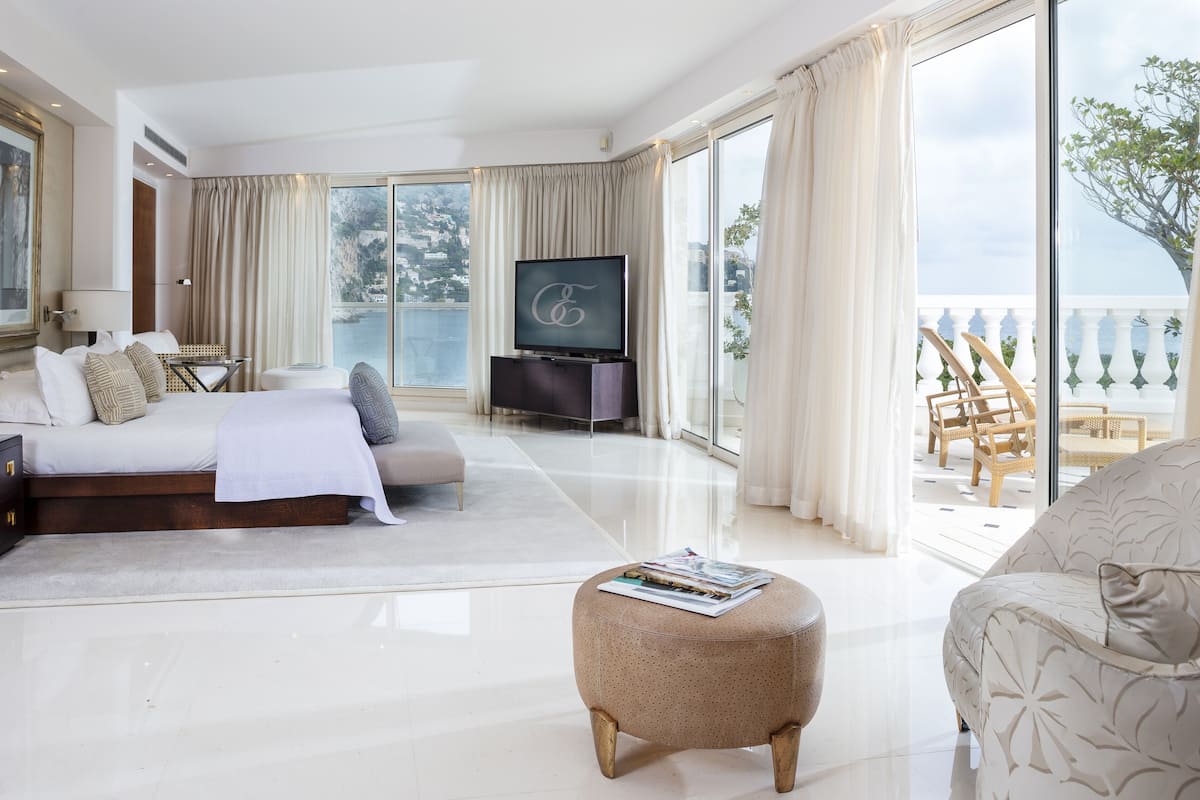 A spacious bedroom with a large bed, a television, and a balcony with a view of the sea.