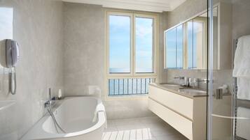 A modern bathroom with a freestanding bathtub, a large mirror, and a view of the sea through a large window.