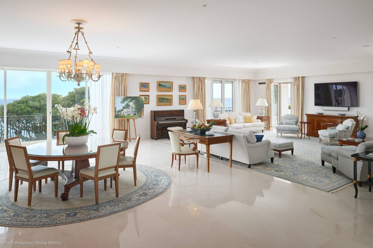 A spacious living room with a piano, a dining area with a round table, and a large TV on the wall.