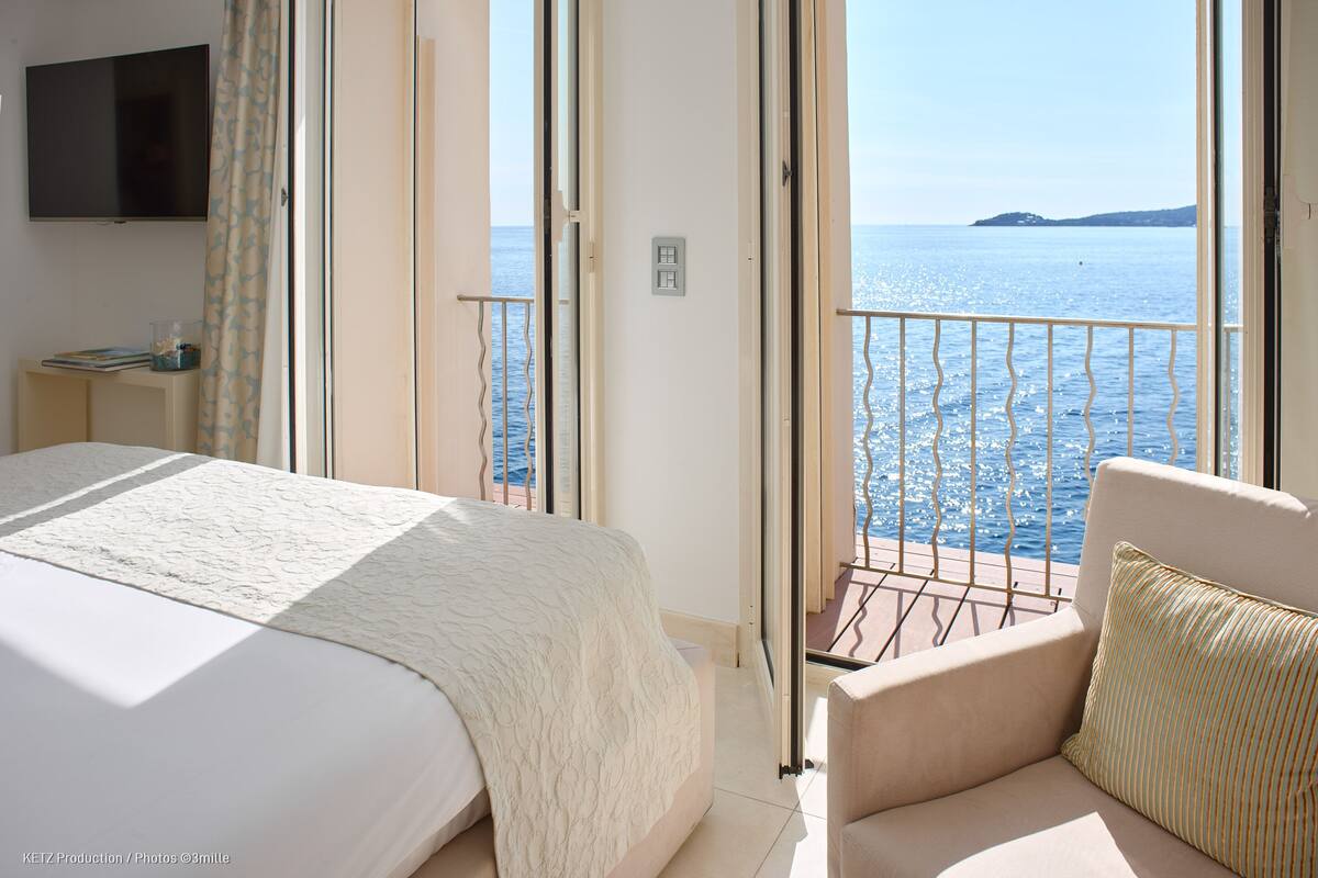 A bedroom with a large bed, a TV, and a balcony with a view of the sea.