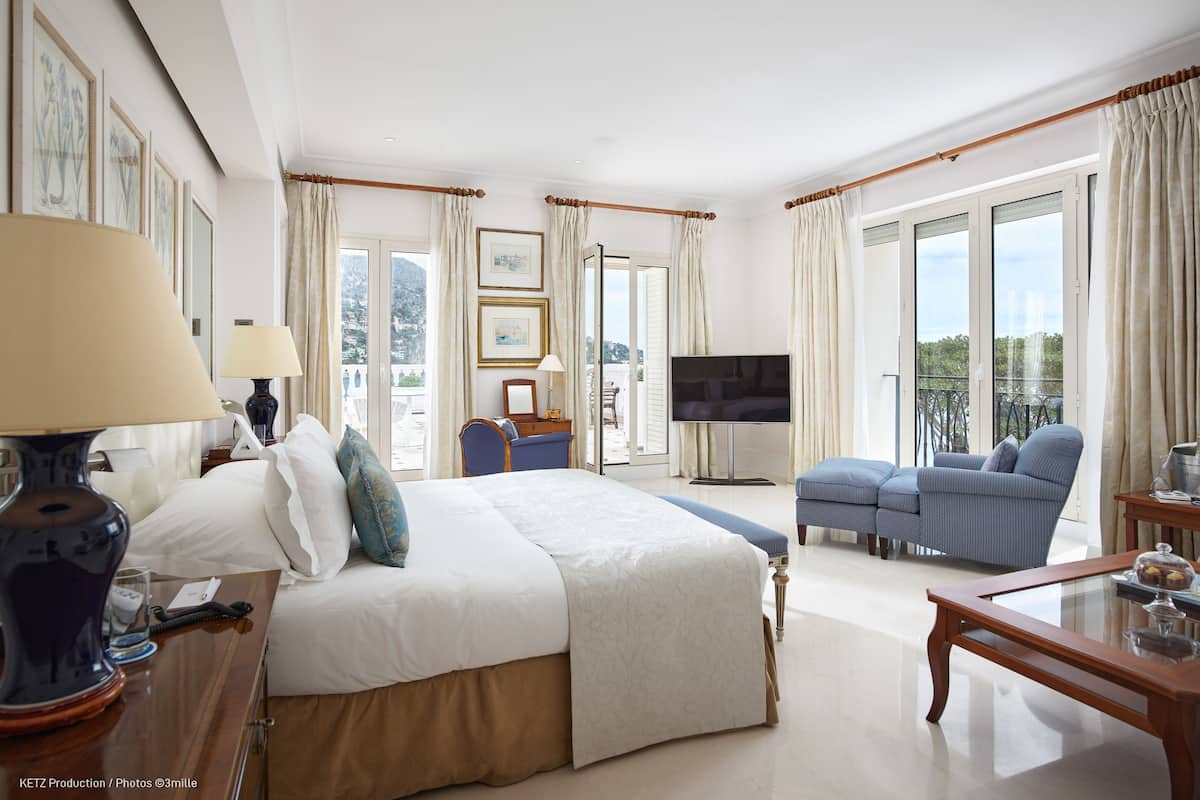 A hotel room with a large bed, a TV, a sofa, and a balcony with curtains.