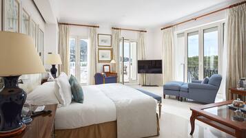 Habitación de hotel con una cama grande, televisión, sofá y balcón con cortinas.