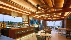 A spacious bar area with wooden beams, a bar counter, and seating arrangements. - Hôtel Cap-Estel (Èze)