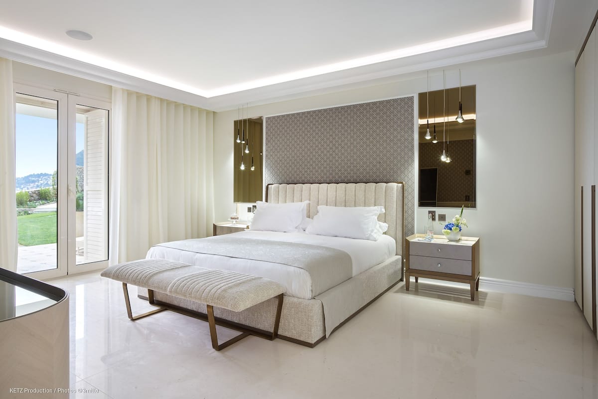 A modern bedroom with a large bed, bedside tables, a bench, and a view of the outdoors.