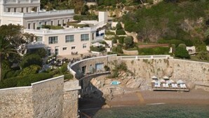 A coastal hotel with a stone facade, a curved entrance, and a beach area with umbrellas. - Hôtel Cap-Estel (Èze)
