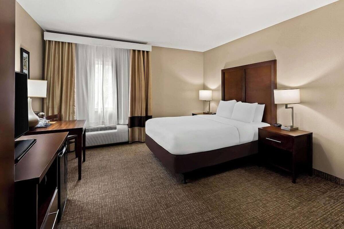 A hotel room with a large bed, two bedside tables with lamps, a desk with a chair, and a television.