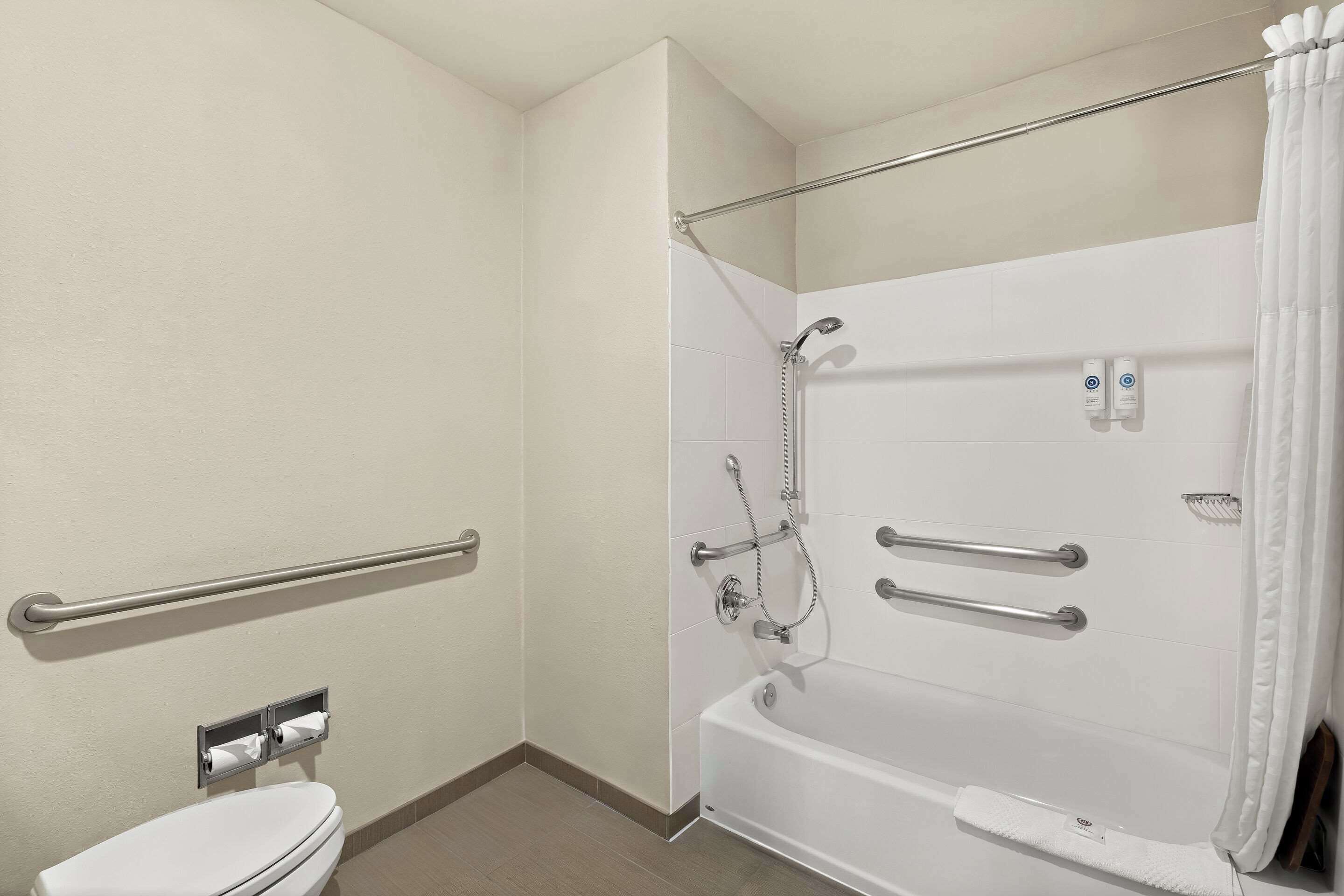 A bathroom with a white toilet, a bathtub with a showerhead, and handrails.