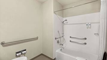 A bathroom with a white toilet, a bathtub with a showerhead, and handrails.