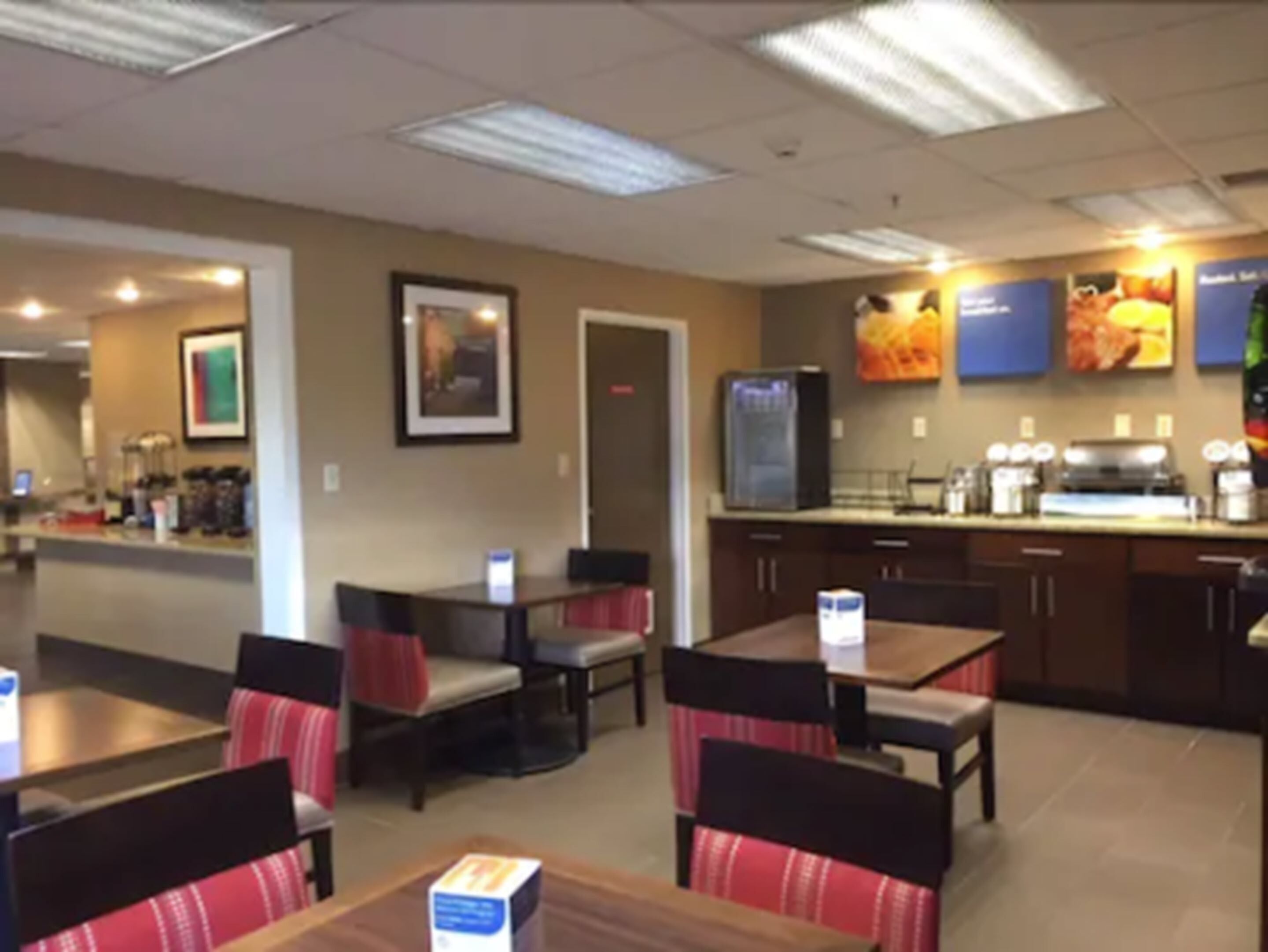 Un restaurant avec des banquettes et des tables, un comptoir avec un réfrigérateur et un tableau affichant le menu.