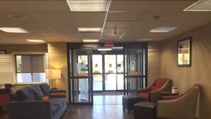 Un hall con mostrador de recepción, dos sillones, un sofá y una puerta que da al exterior.
