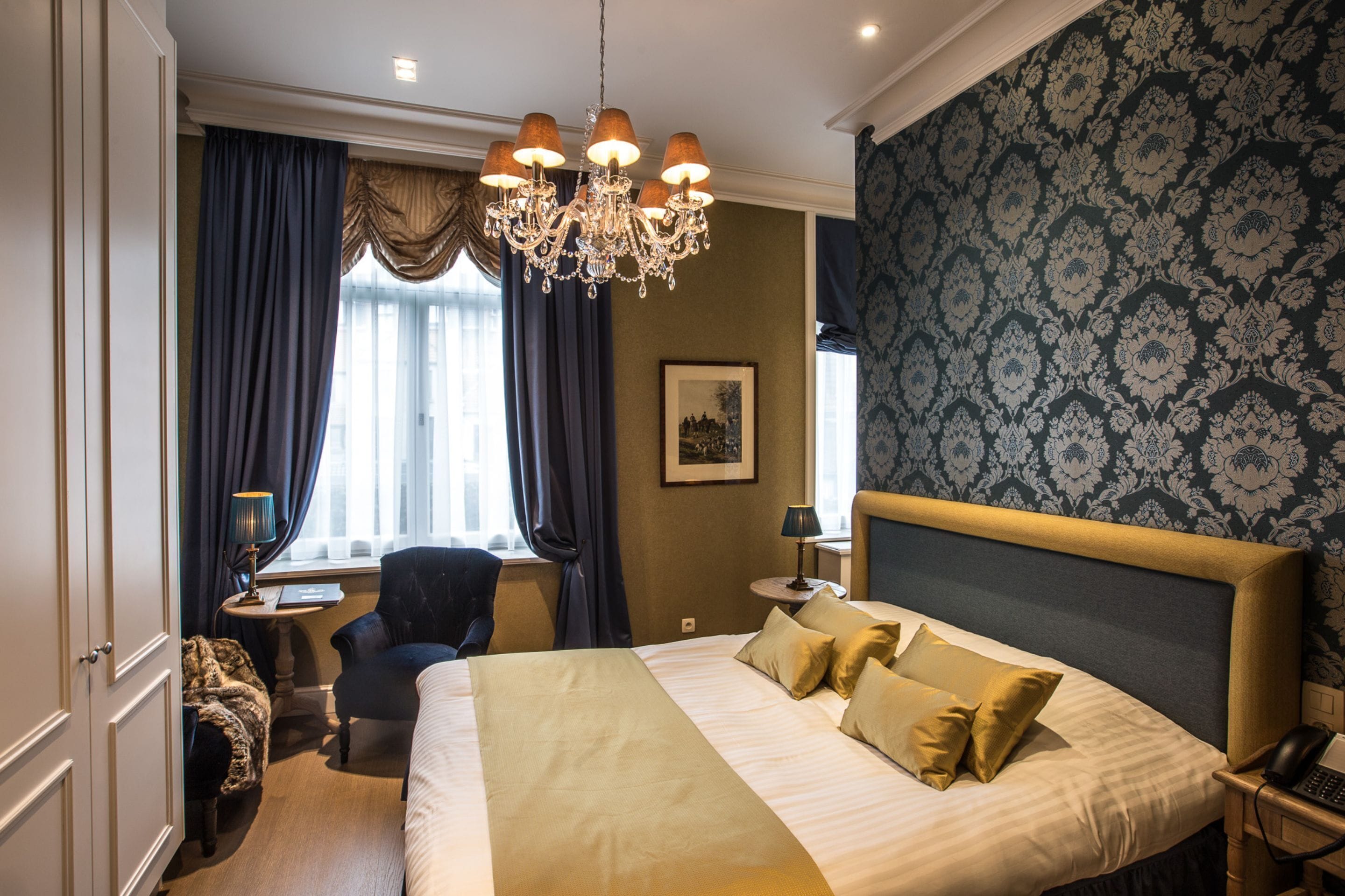 Une chambre d’hôtel avec un grand lit, un bureau, une chaise, un lustre et un papier peint à motifs.