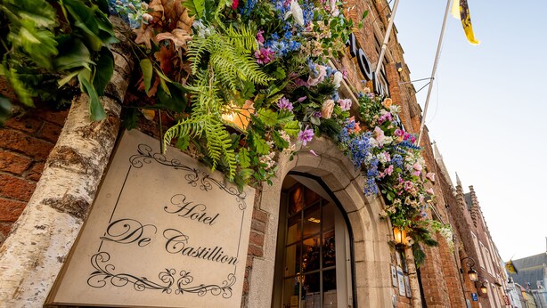 A hotel entrance with a sign reading "Hotel De Castillion," surrounded by lush greenery and flowers. - Hotel de Castillion (Bruges)