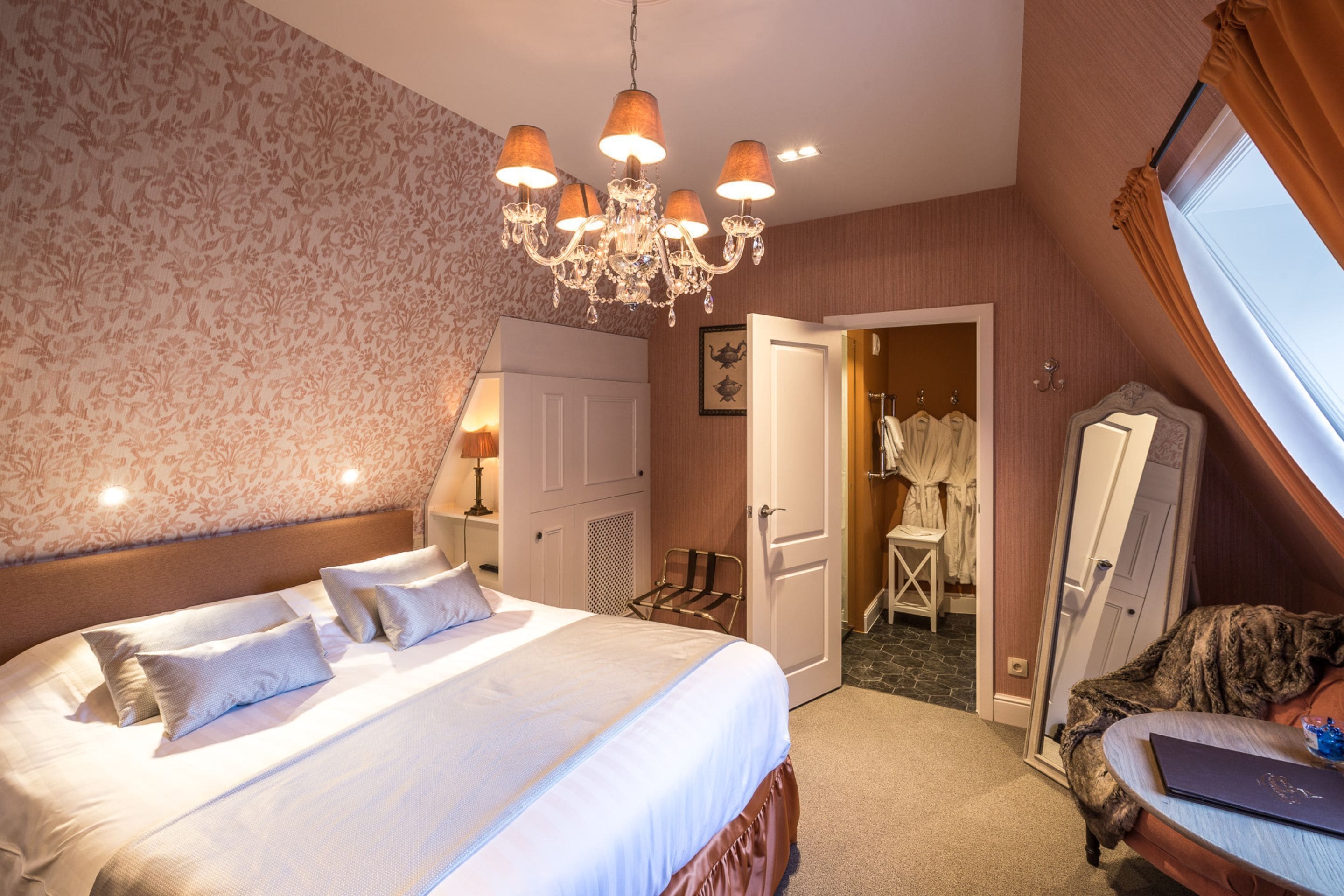 A hotel room with a large bed, a chandelier, a wardrobe, and a mirror.