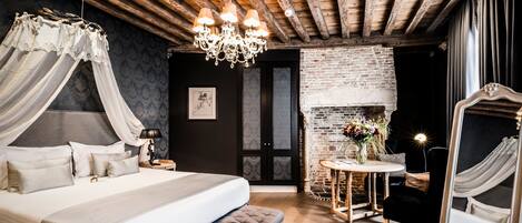 Een slaapkamer met een groot bed, een bankje, een kroonluchter, een open haard en een spiegel.