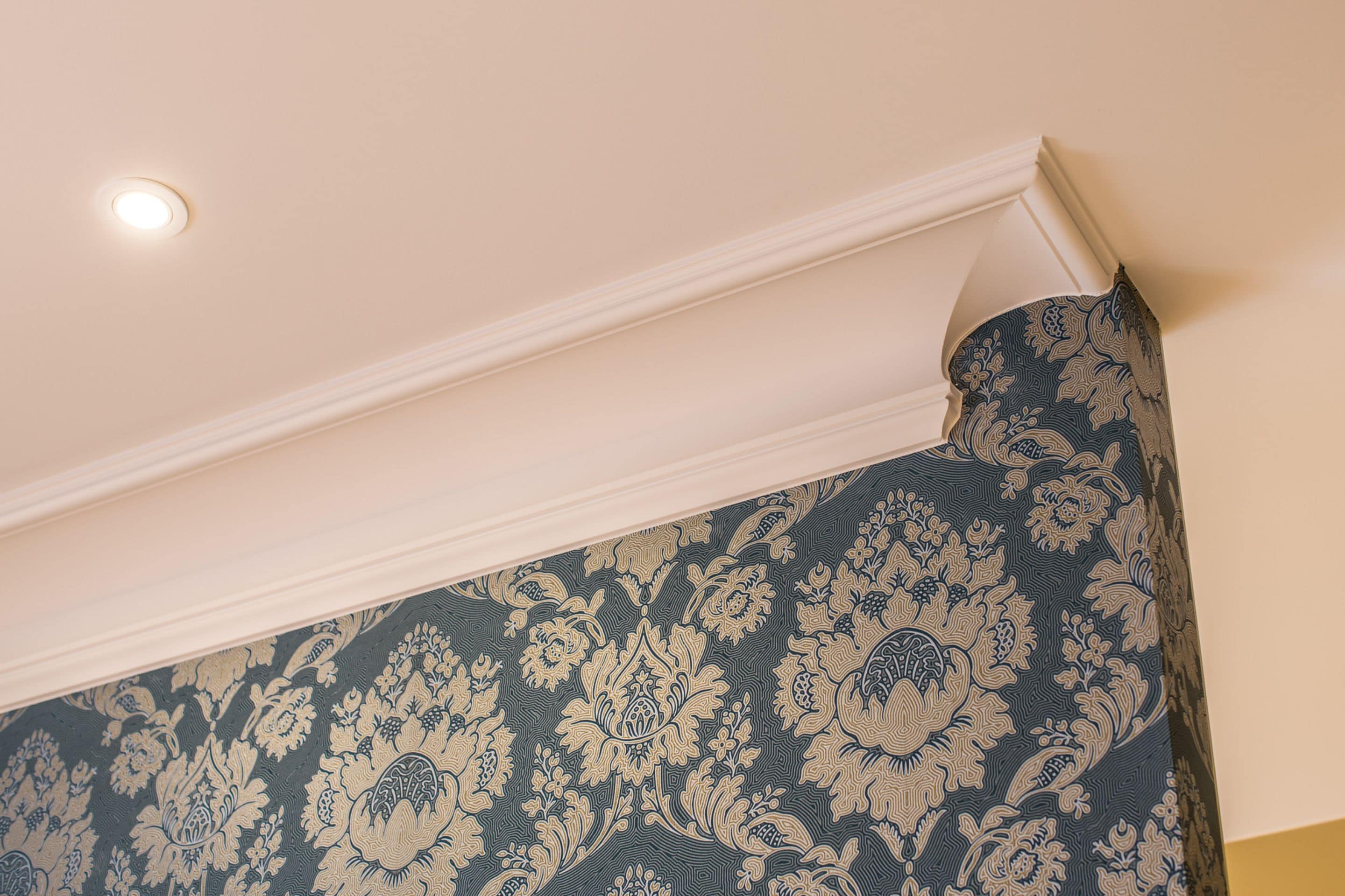 A corner of a room with a patterned wallpaper and a white ceiling with a recessed light.