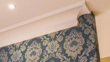 A corner of a room with a patterned wallpaper and a white ceiling with a recessed light.