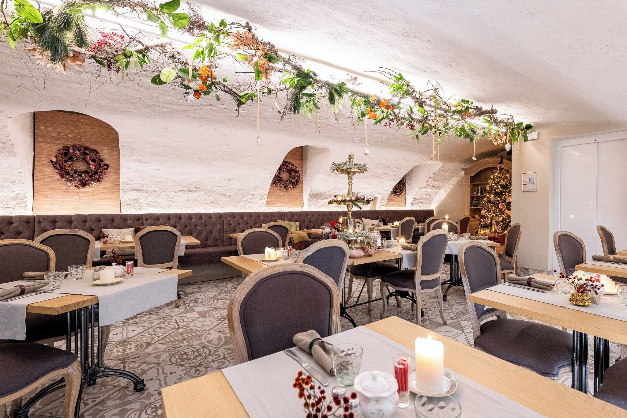 A restaurant with a rustic interior, featuring wooden tables, cushioned seating, and decorative plants hanging from the ceiling.