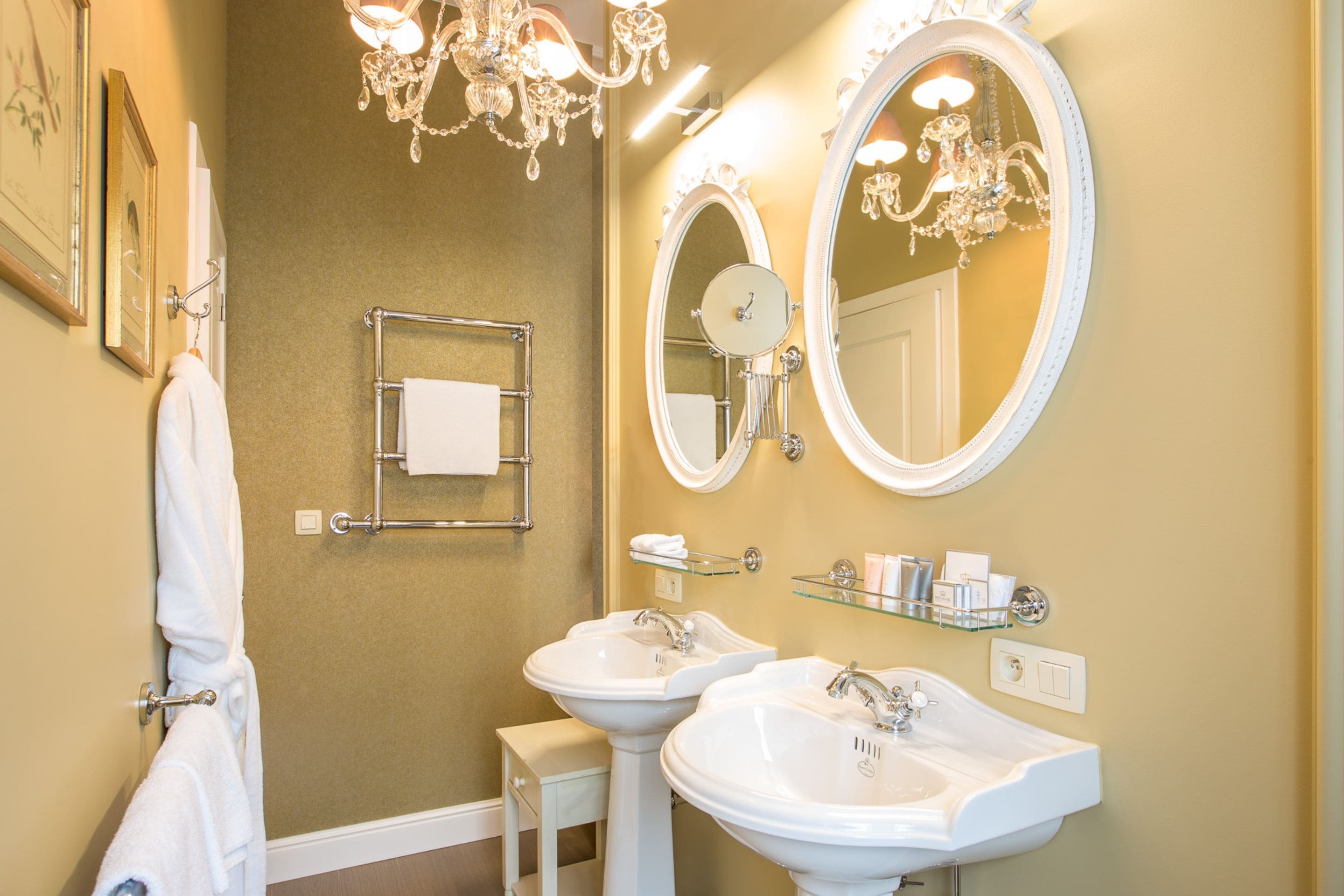A bathroom with two sinks, a mirror, a chandelier, and a towel rack.