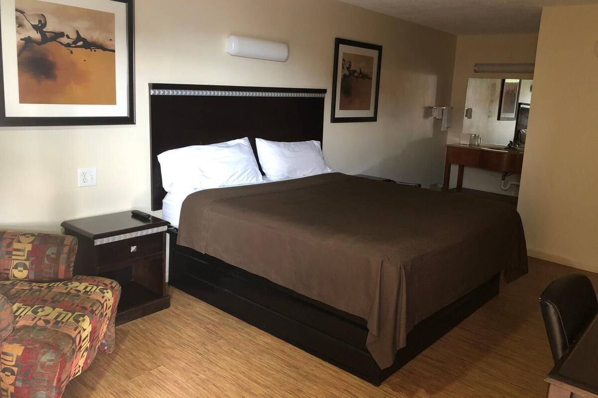 A hotel room with a large bed, a nightstand, a chair, and a bathroom visible through an open door.