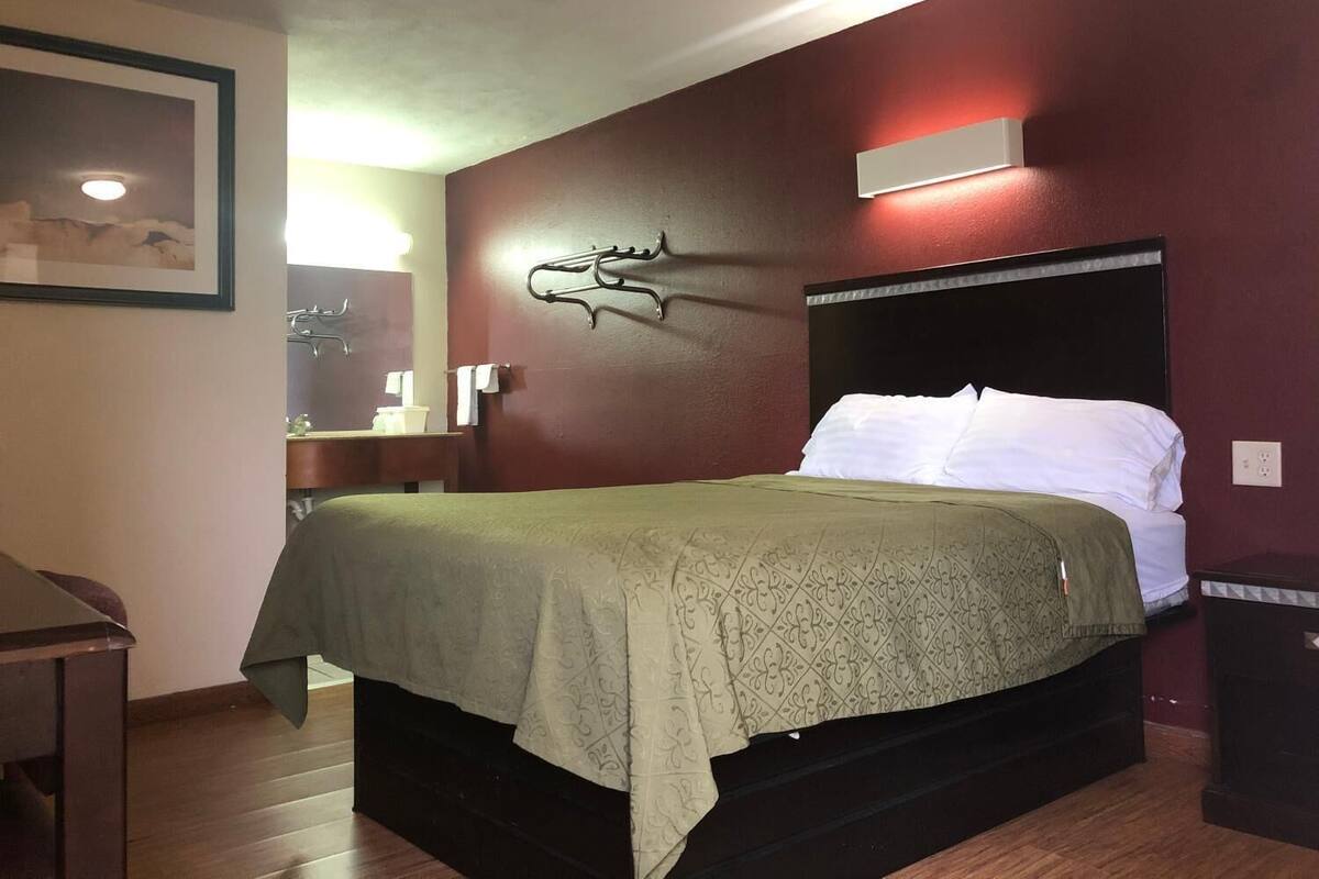 A hotel room with a bed, a nightstand, a wall-mounted light, and a framed picture on the wall.