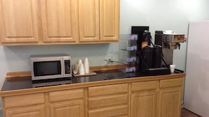 A kitchen with wooden cabinets, a microwave, a coffee machine, and disposable cups.