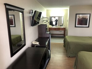 Camera d'albergo con un letto, una scrivania con un telefono, uno specchio, una TV e un bagno visibile sullo sfondo.