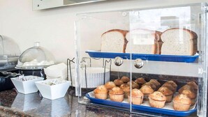 A breakfast buffet with bread, muffins, and a coffee station. - Castle Inn & Suites (Niagara Falls)