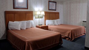 A hotel room with two beds, each with brown bedding and white pillows, a nightstand with a lamp, and two framed pictures on the wall. - Castle Inn & Suites (Niagara Falls)