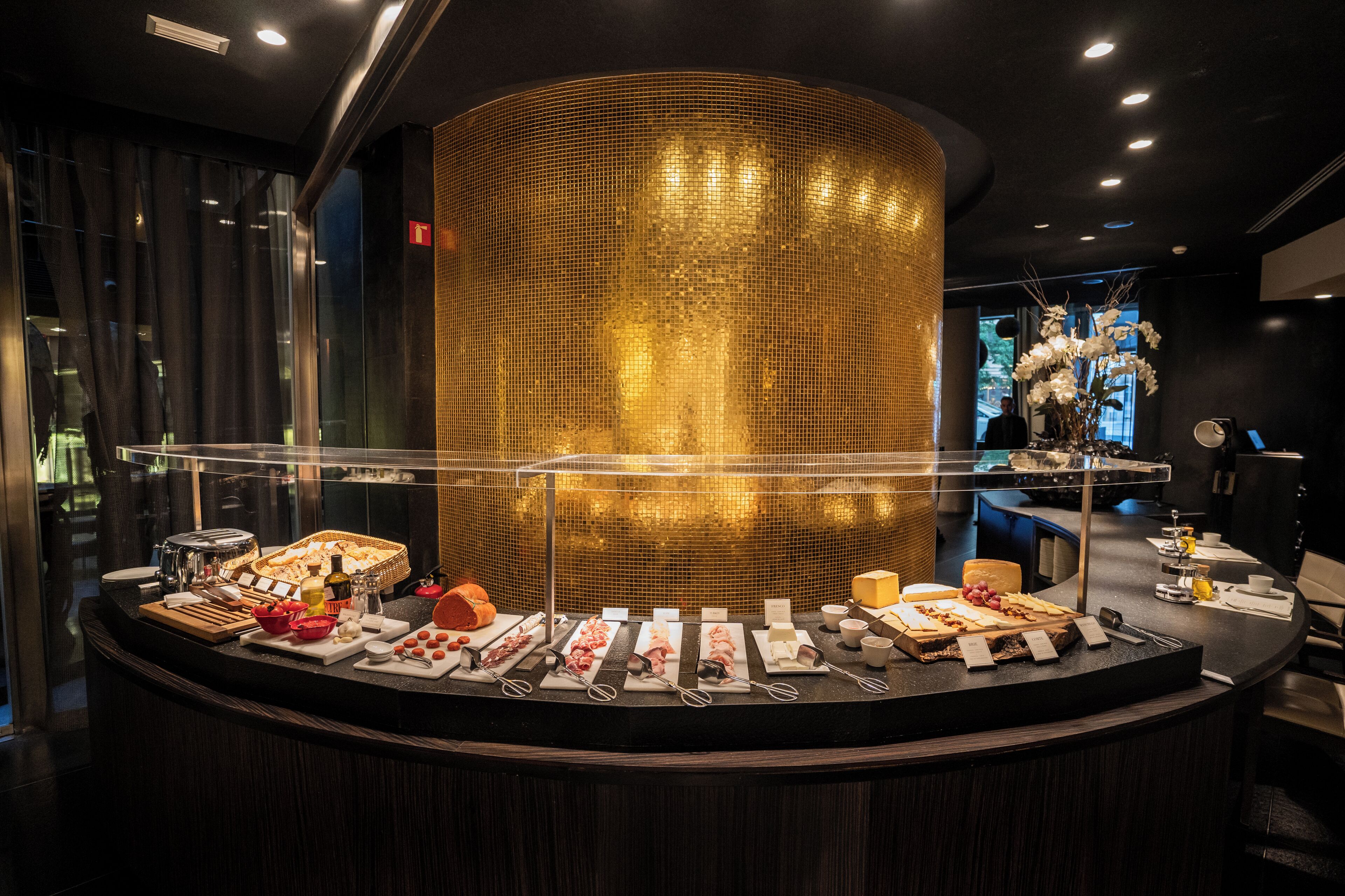 Balcão de buffet com diversos alimentos e utensílios, uma estrutura dourada decorativa em tela e design de interiores moderno.