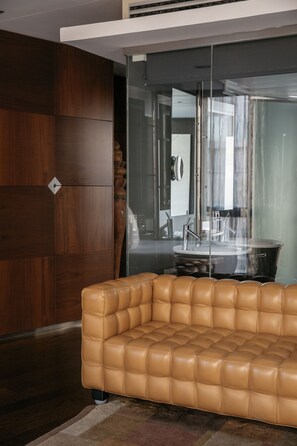 A modern living room with a leather sofa, wooden panel walls, and a glass partition separating the living area from a dining space.