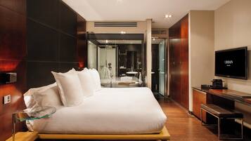 Une chambre d’hôtel moderne dotée d’un grand lit, d’une télévision, d’un bureau et d’une salle de bain visible à travers une paroi en verre.